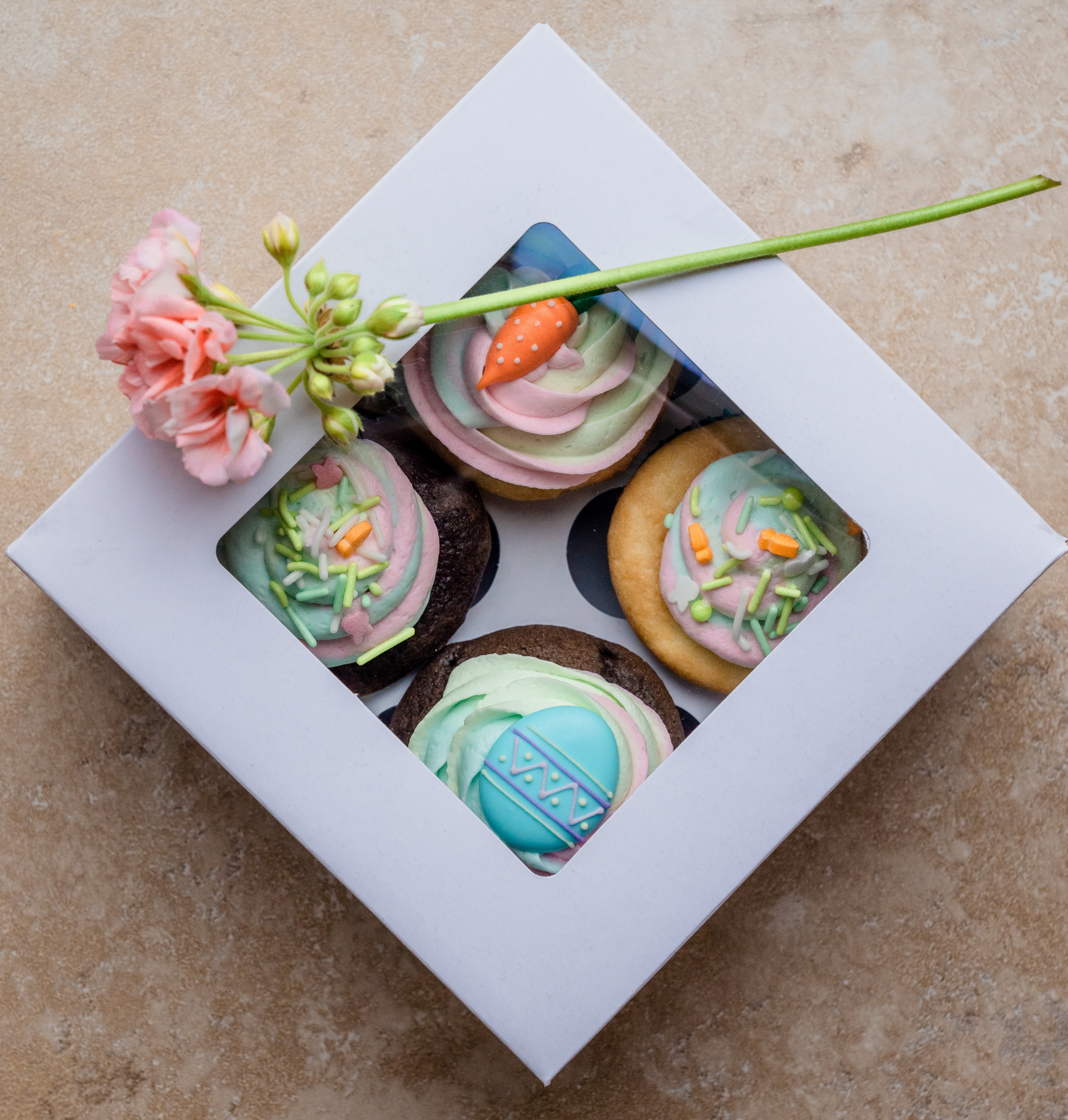 A cute cardboard box of Easter-themed cupcakes, with a stem of pink blossoms lying on top.